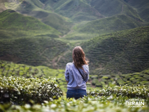 A woman standing alone at the top of a mountain in an isolated, rural area.